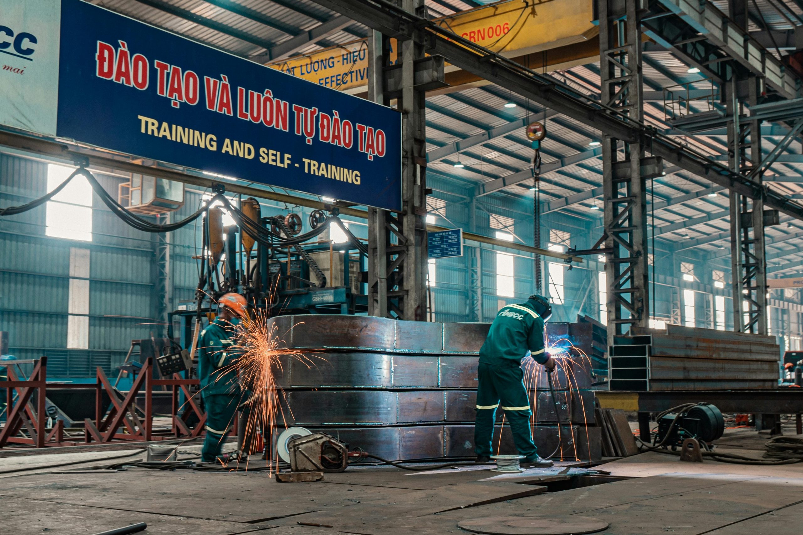Tư vấn pháp luật lao động: Quyền lợi người lao động cần biết Workers weld metal structures in a bustling industrial factory, showcasing a dynamic work environment.