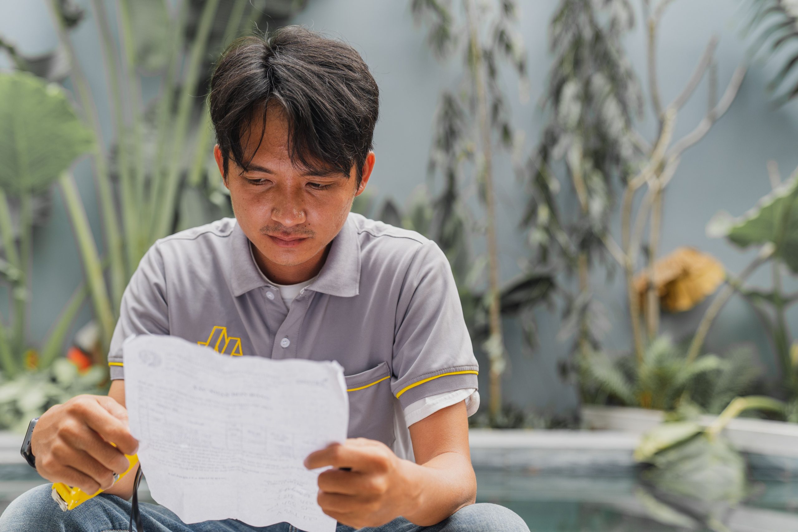 Asian man attentively reading a document in an outdoor setting in Hồ Chí Minh, Vietnam.