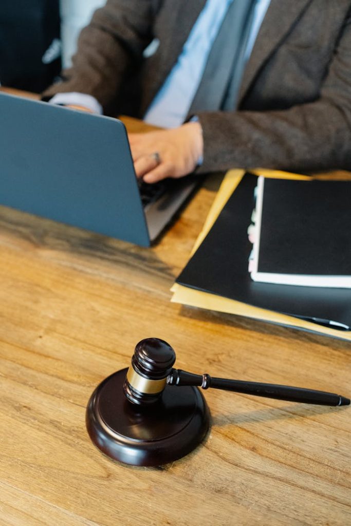 pexels photo 5668802 From above of crop anonymous male lawyer in formal clothes typing on laptop while sitting at wooden table with stack of documents and gavel