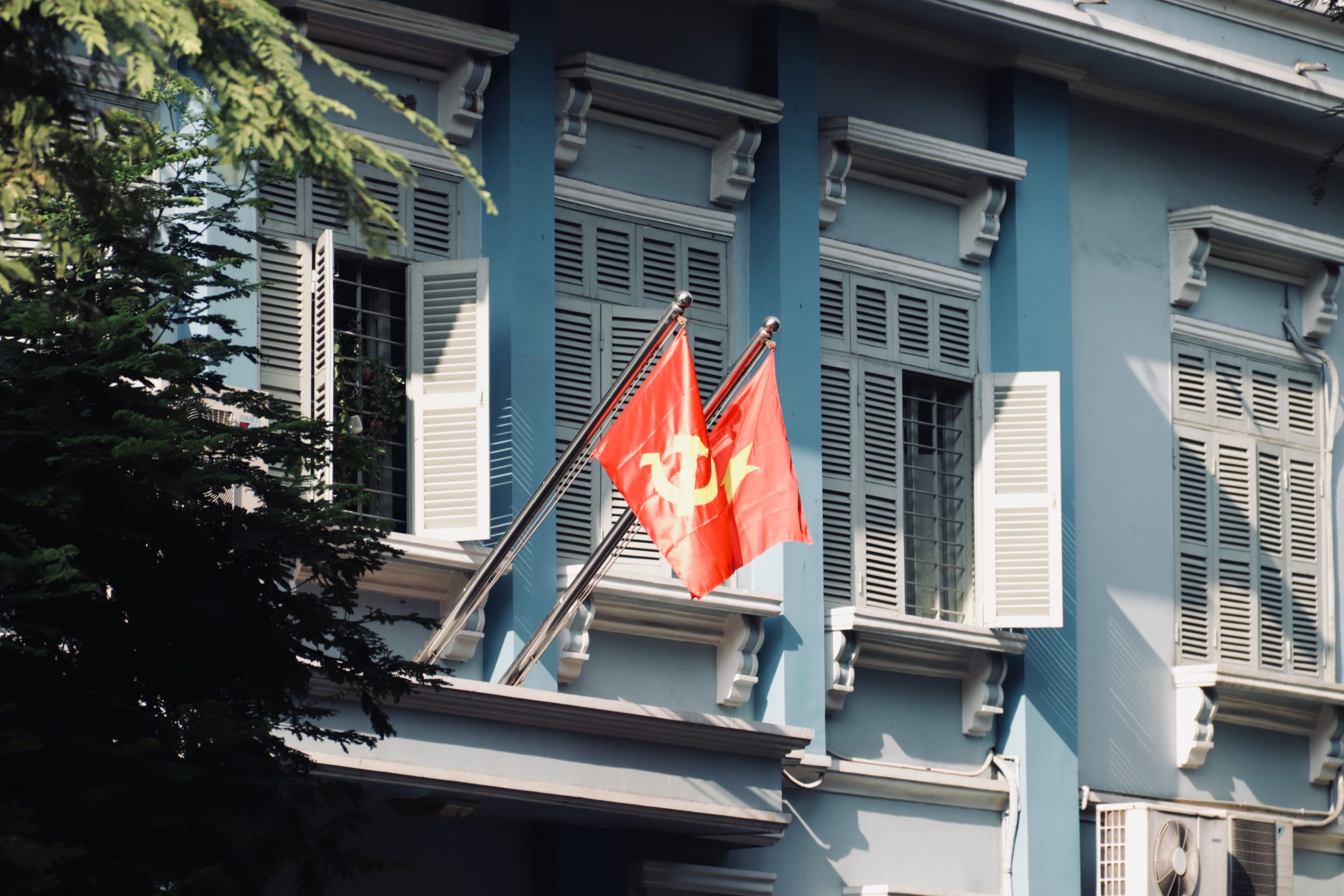 Close-up of a historic building facade with communist flags waving in sunlight.